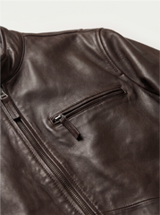 Close-up of a dark brown leather jacket showing a zippered pocket and part of the front zipper, photographed against a light neutral background.