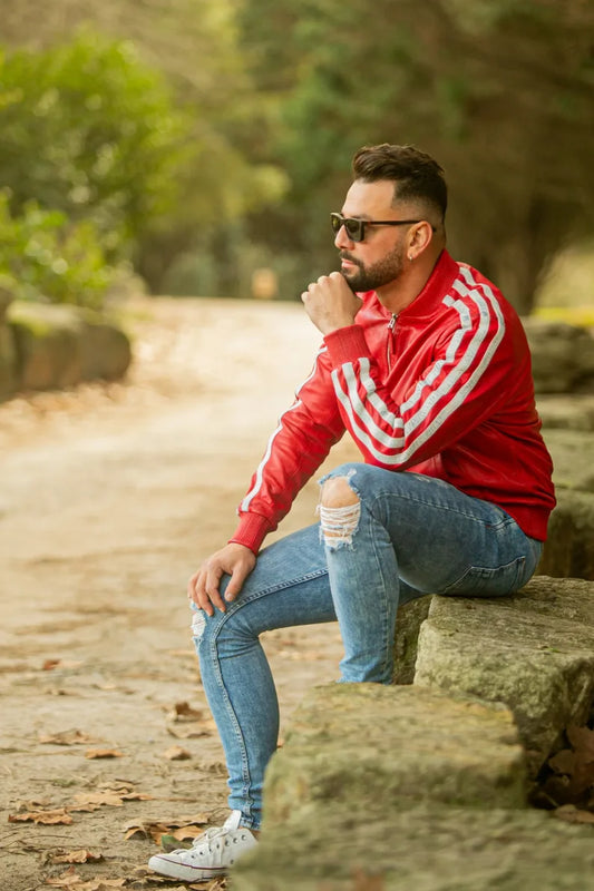 Men's Roma red leather jacket outdoor lifestyle shot, model seated on stone wall, white stripe sleeve