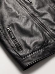 Close-up of a black leather jacket showing the texture of the leather, a zippered pocket, and a main zipper on a light gray background.