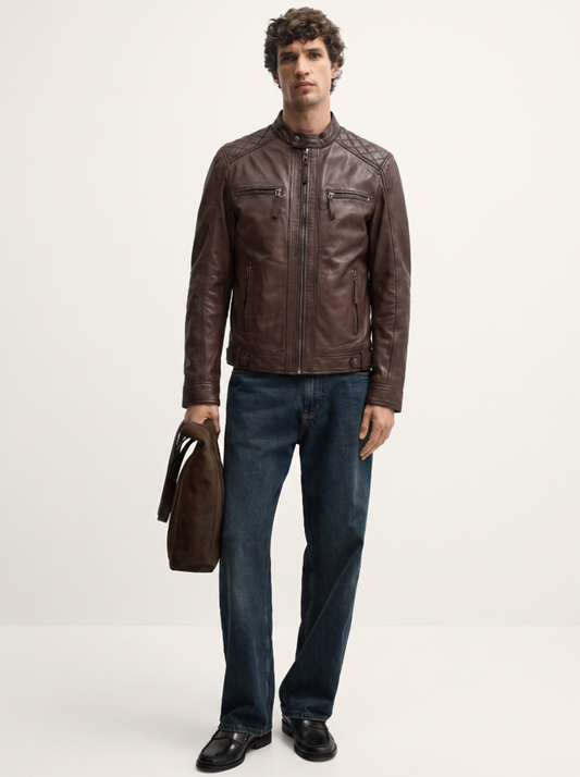 A man modeling a dark brown leather jacket, paired with dark blue jeans, black shoes, and holding a brown leather briefcase against a plain light background.